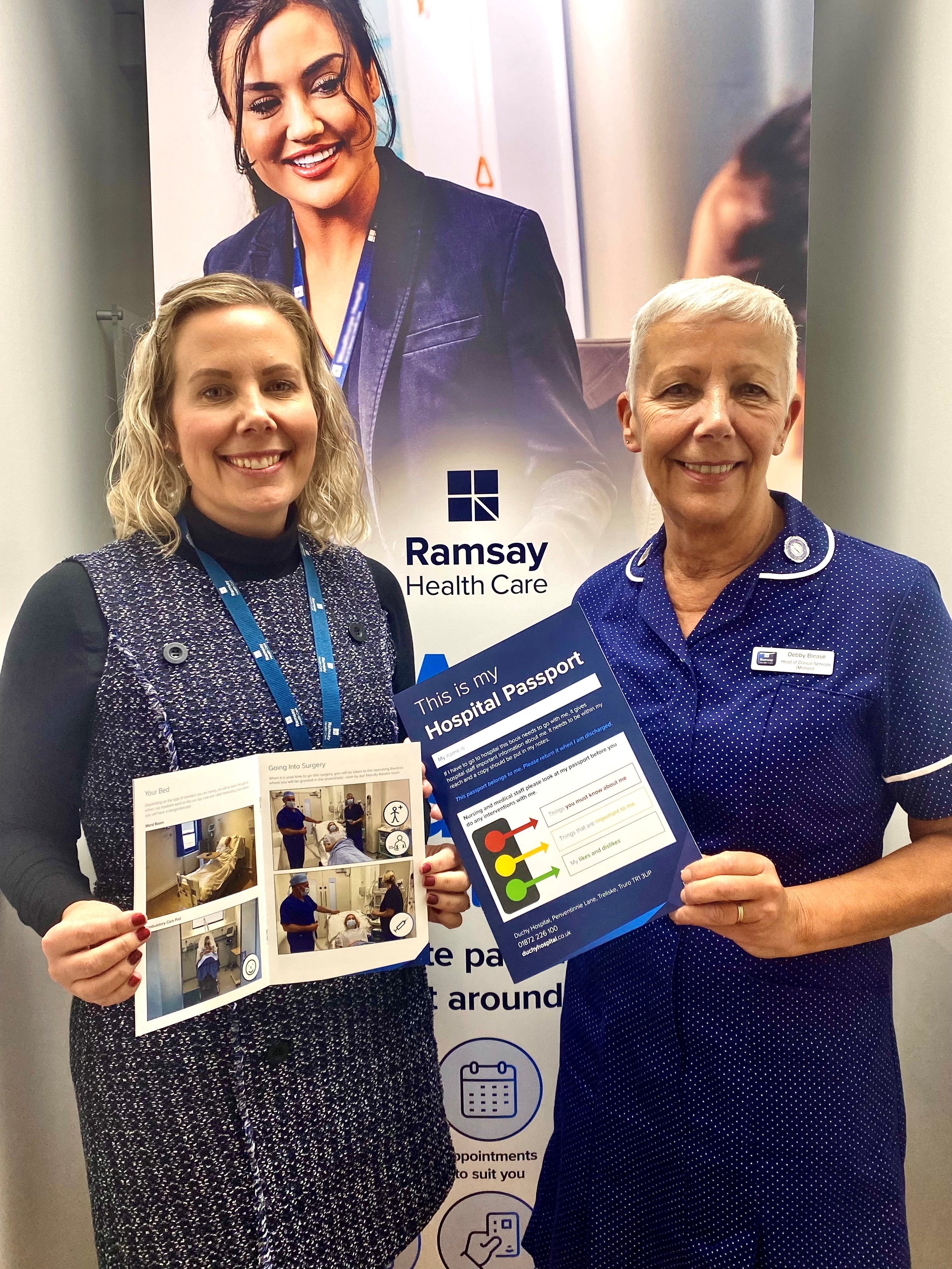 Debby Blease and Jo Larcome from Duchy Hospital holding a patient passport smiling