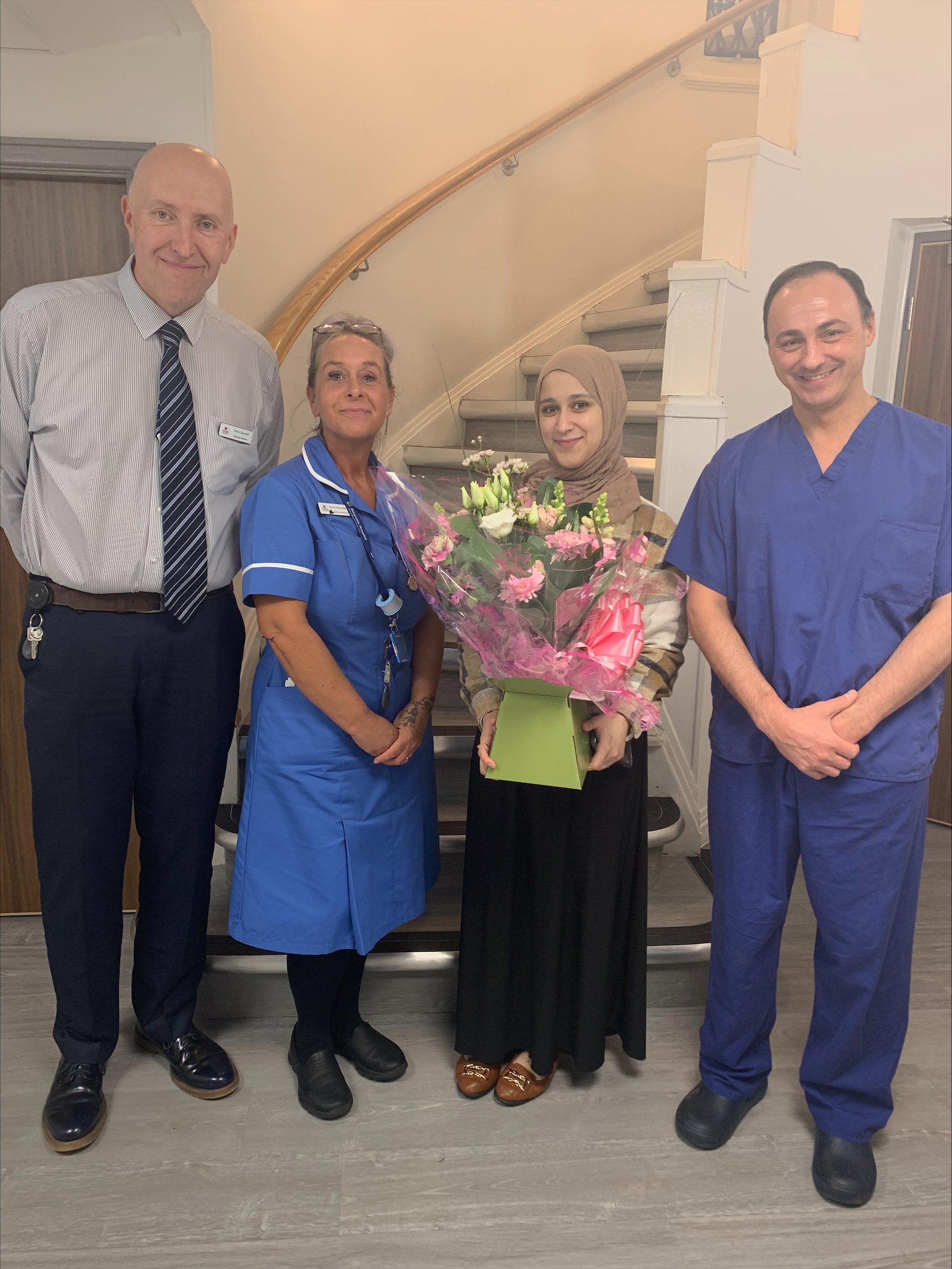 three staff members with patient holding a bunch of flowers